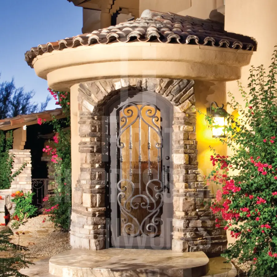 A hand-forged iron entry door set in a stone arch on an Arizona home at dusk